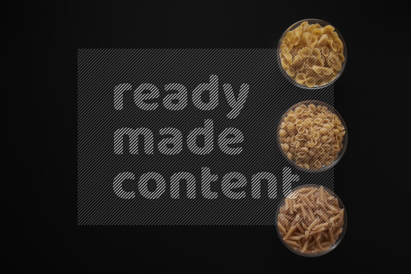 Different pasta types in 3 glass bowls on black background