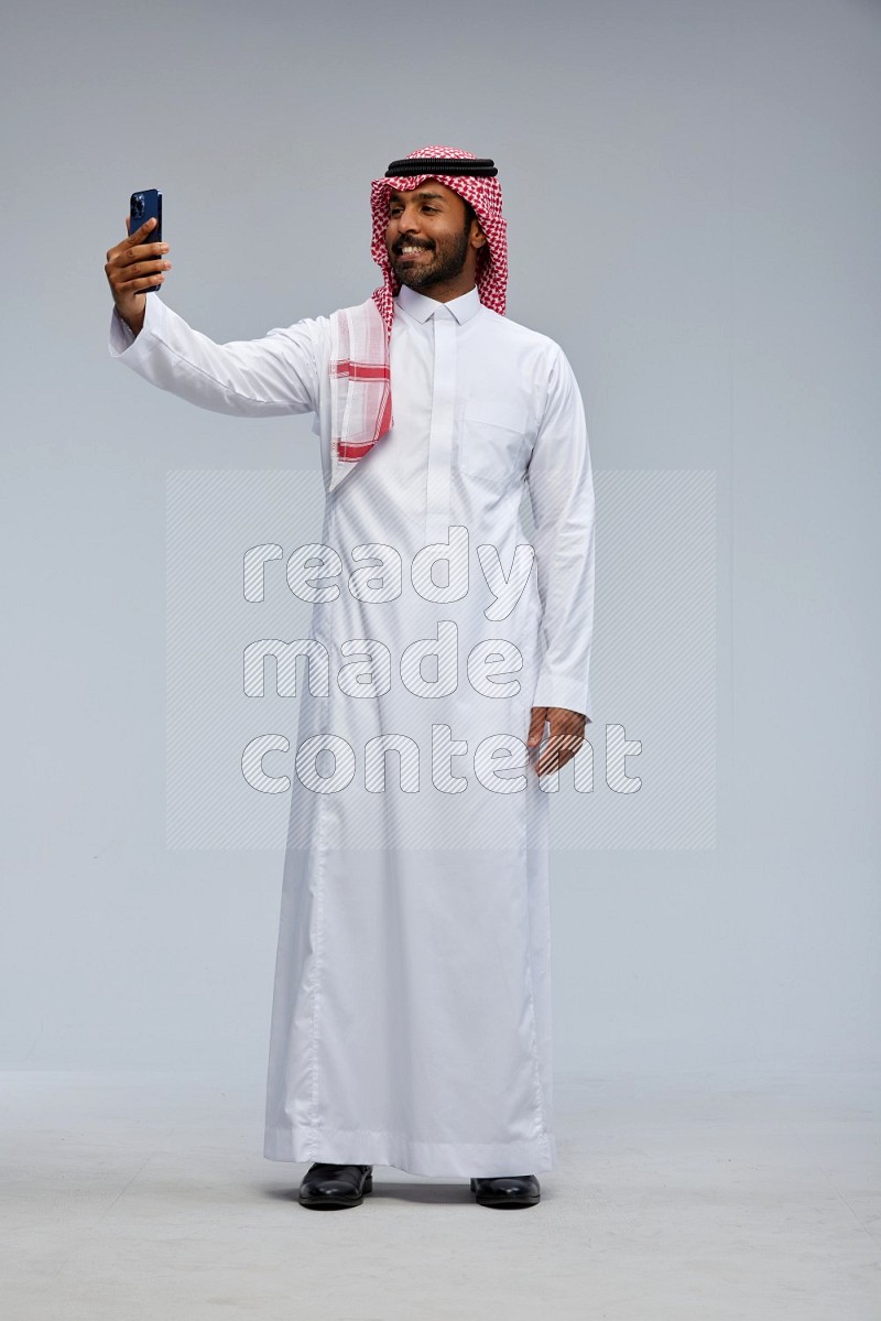 Saudi man Wearing Thob and shomag standing taking selfie on Gray background