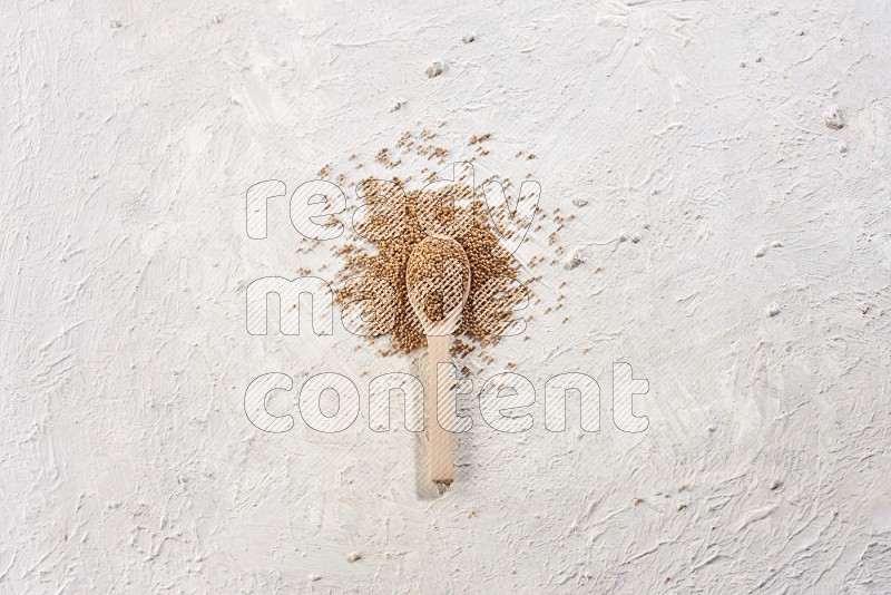 A wooden spoon full of mustard seeds on a textured white flooring