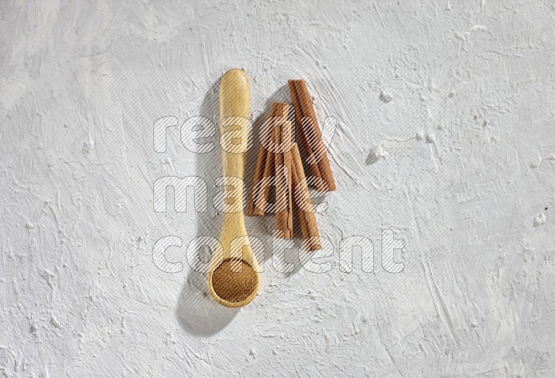 بودرة القرفة في ملعقة خشبية مع أعواد القرفة على خلفية بيضاء