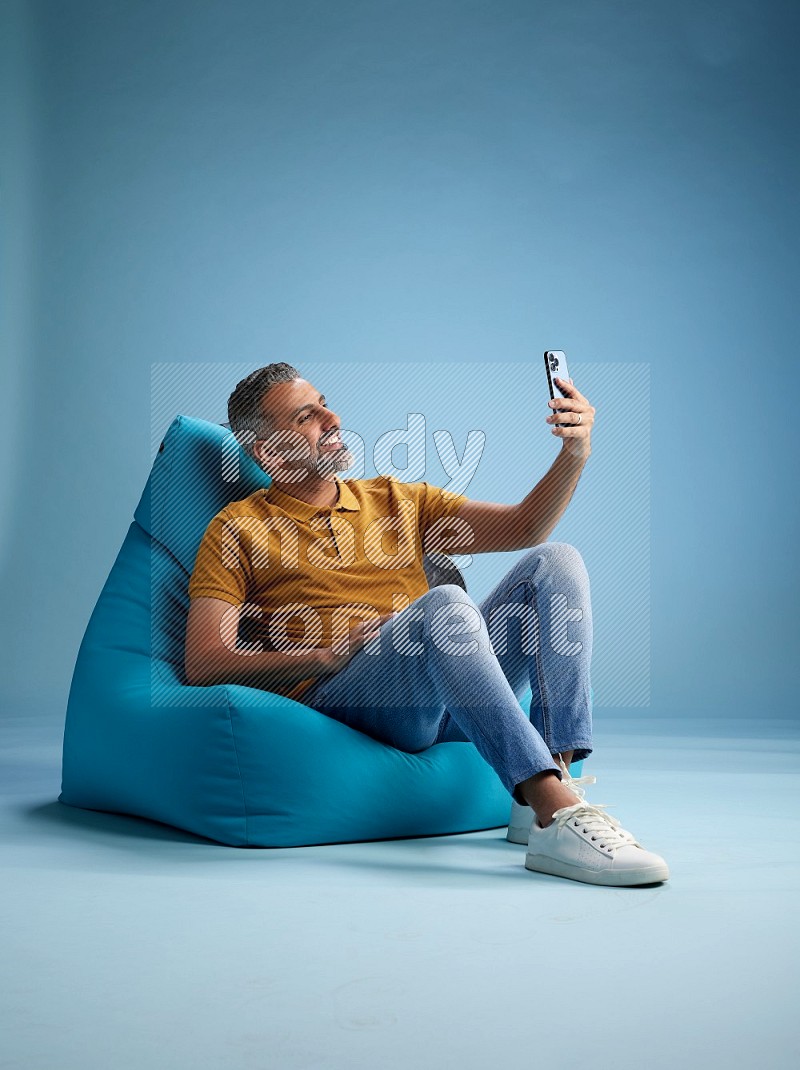 A man sitting on a blue beanbag and taking selfie