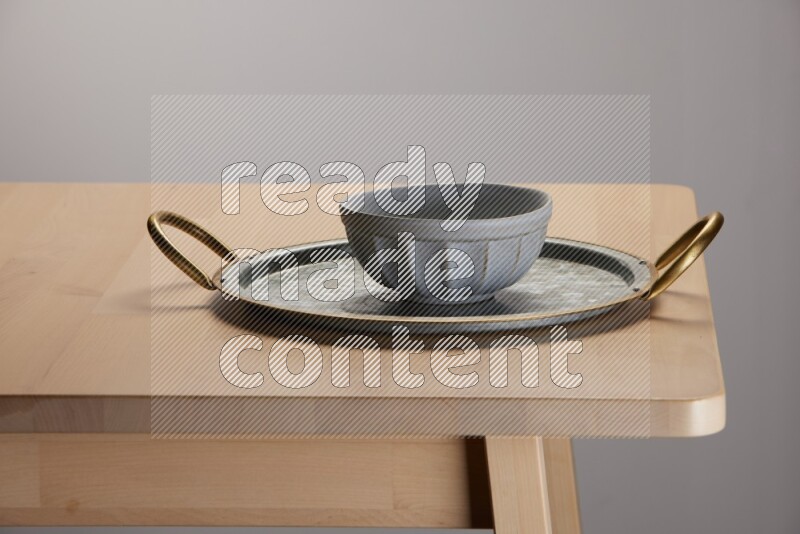 grey bowl placed on a rounded stainless steel tray with golden handels on the edge of wooden table