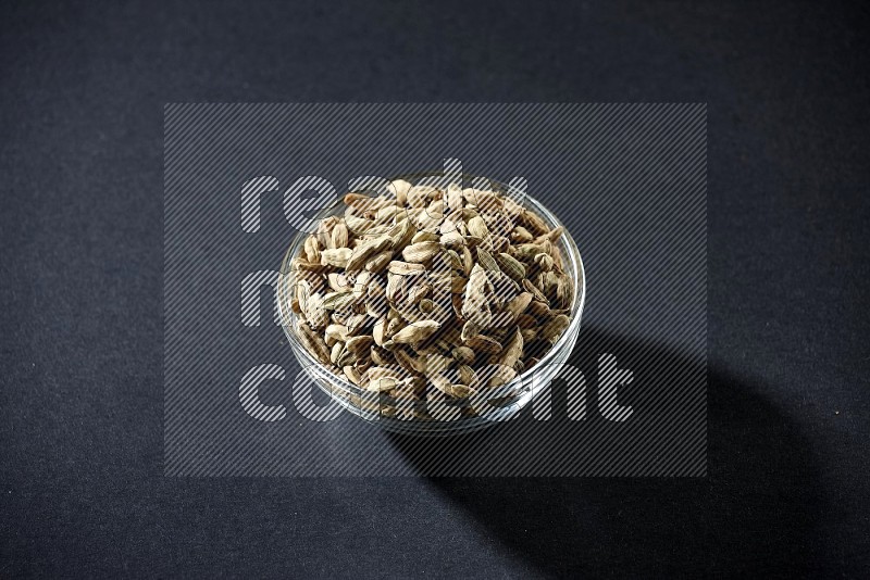 A glass bowl full of cardamom on black flooring