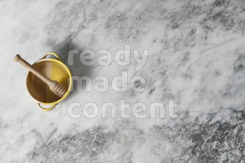 Multicolored pottery bowl with wooden honey dipper in it on grey marble background