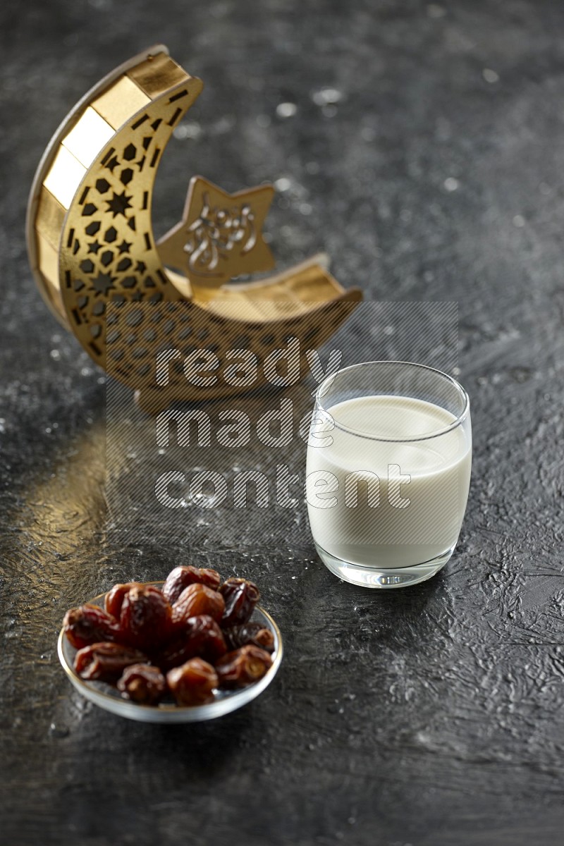 A crescent lantern with drinks, dates, nuts, prayer beads and quran on textured black background