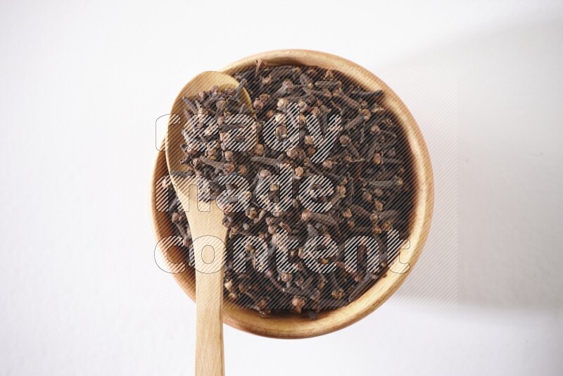 وعاء خشبي وملعقة خشبية ممتلئان بالقرنفل على خلفية بيضاء