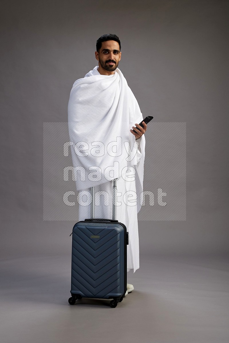 A man wearing Ehram Standing holding traveling bag on gray background