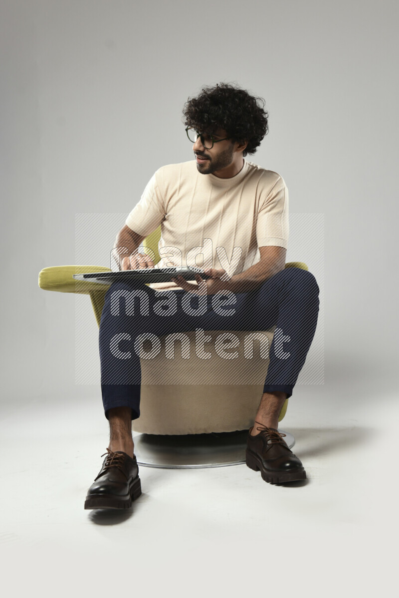 A man wearing casual sitting on a chair holding a laptop on white background