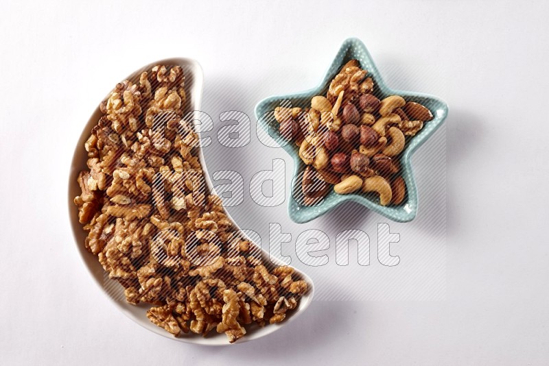 Walnuts in a crescent pottery plate and a star shaped plate with mixed nuts on white background