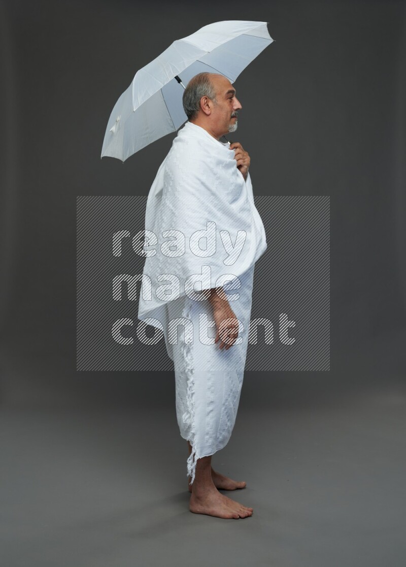 A man wearing Ehram Standing holding umbrella on gray background