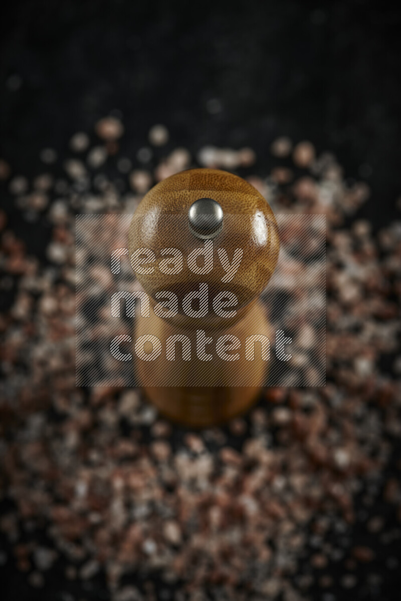 A wooden grinder standing upright and surrounded by coarse pink himalayan salt on black background