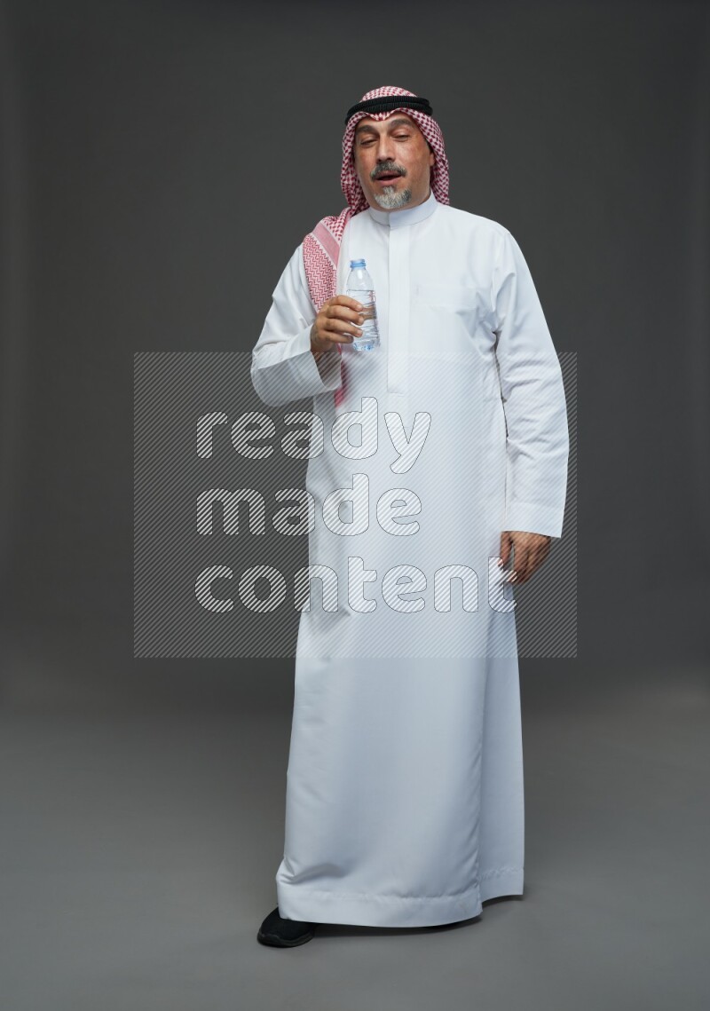 Saudi man with shomag Standing drinking water on gray background