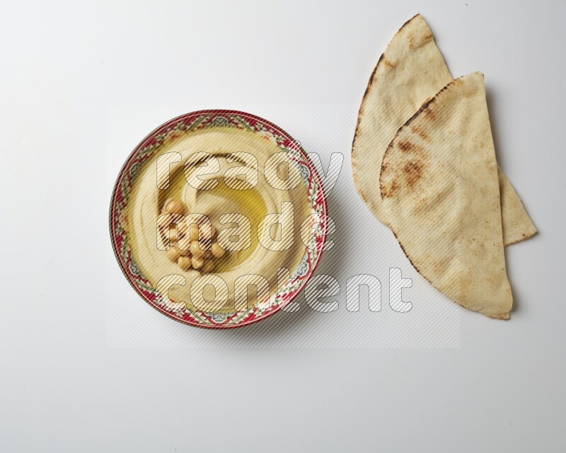 Hummus in a red plate with patterns garnished with roasted chickpeas  on a white background