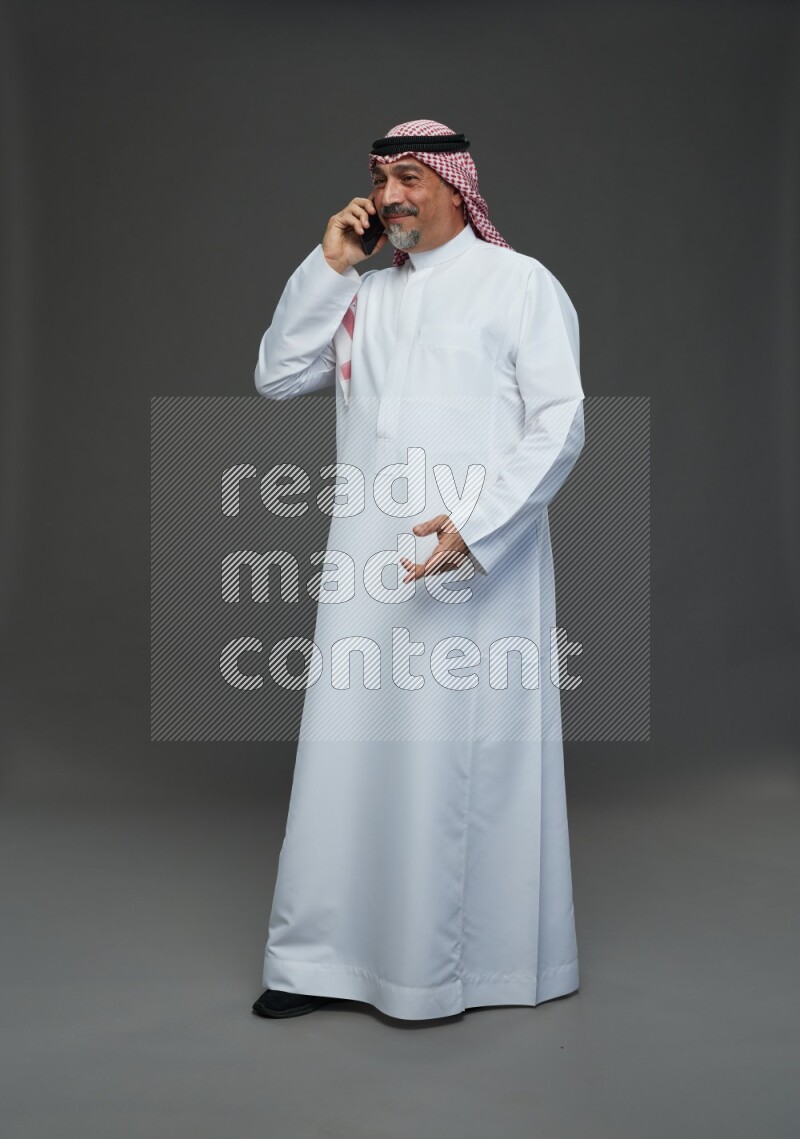 Saudi man with shomag Standing talking on phone on gray background