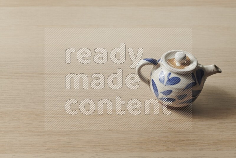A pottery teapot on light wooden background