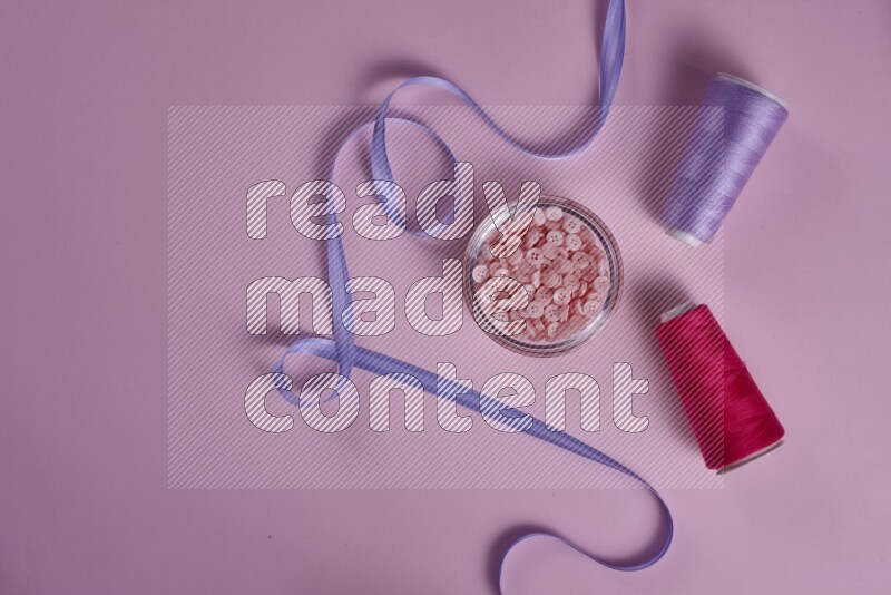 A purple and pink collection of sewing and tailoring tools arranged on a pink background
