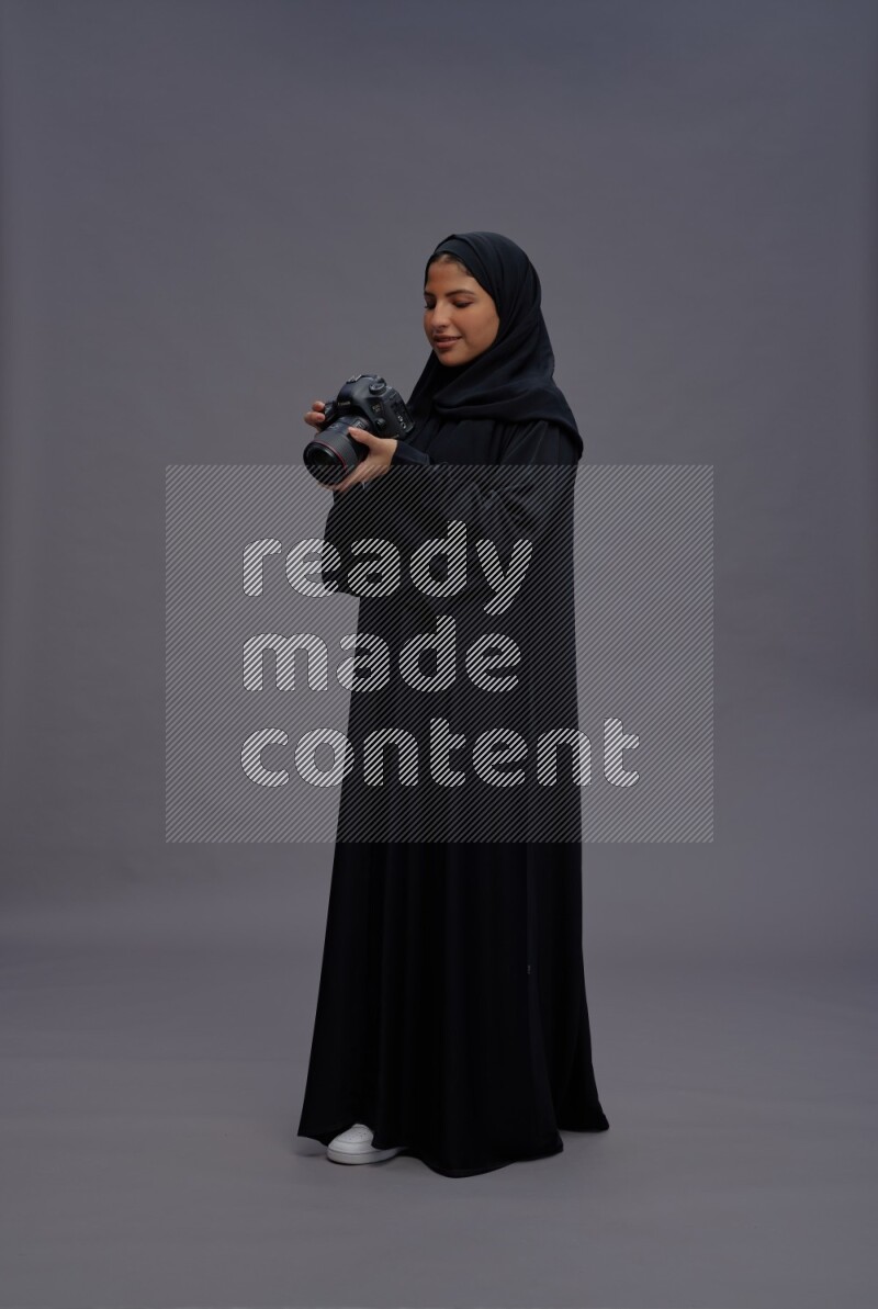 Saudi woman wearing Abaya standing holding Camera on gray background