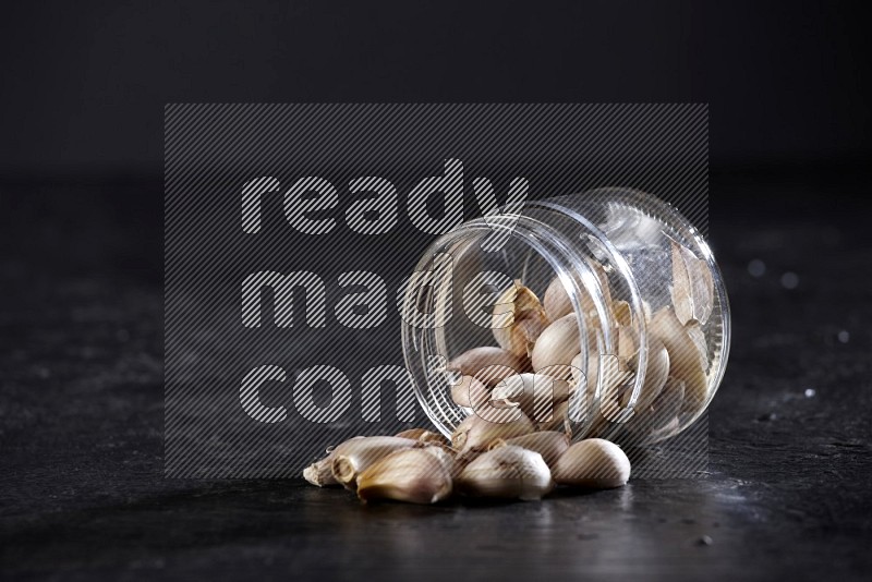 A glass jar full of garlic cloves flipped and the cloves came out on a textured black flooring in different angles
