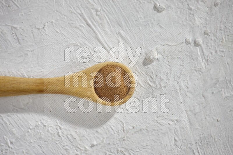 Cinnamon powder in a wooden spoon on a white background