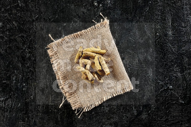 Dried turmeric whole fingers on a burlap piece of fabric on textured black flooring