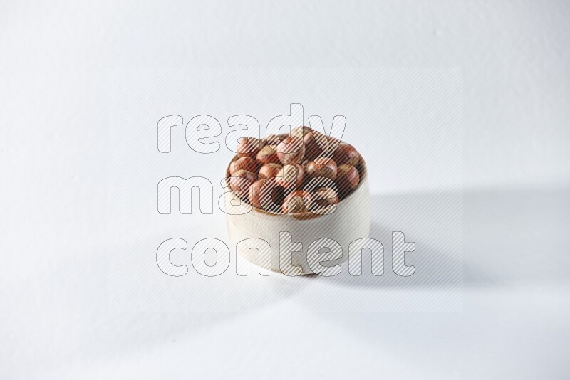 A beige ceramic bowl full of hazelnuts on a white background in different angles