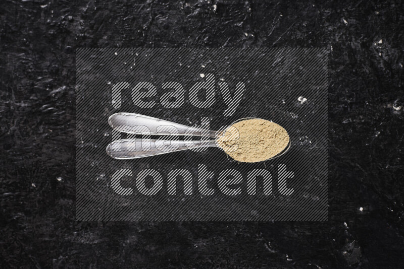 Two metal spoons full of ground ginger powder on black background