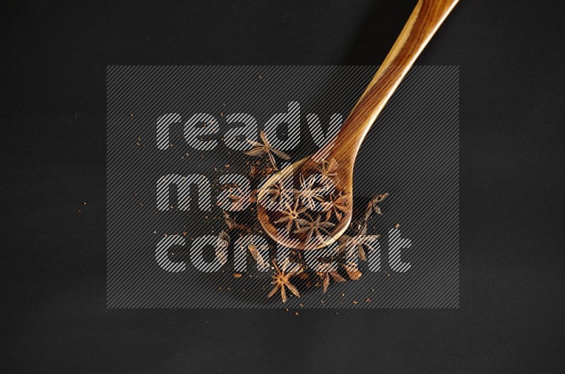 Star Anise in a wooden spoon ladle with more anise on black flooring