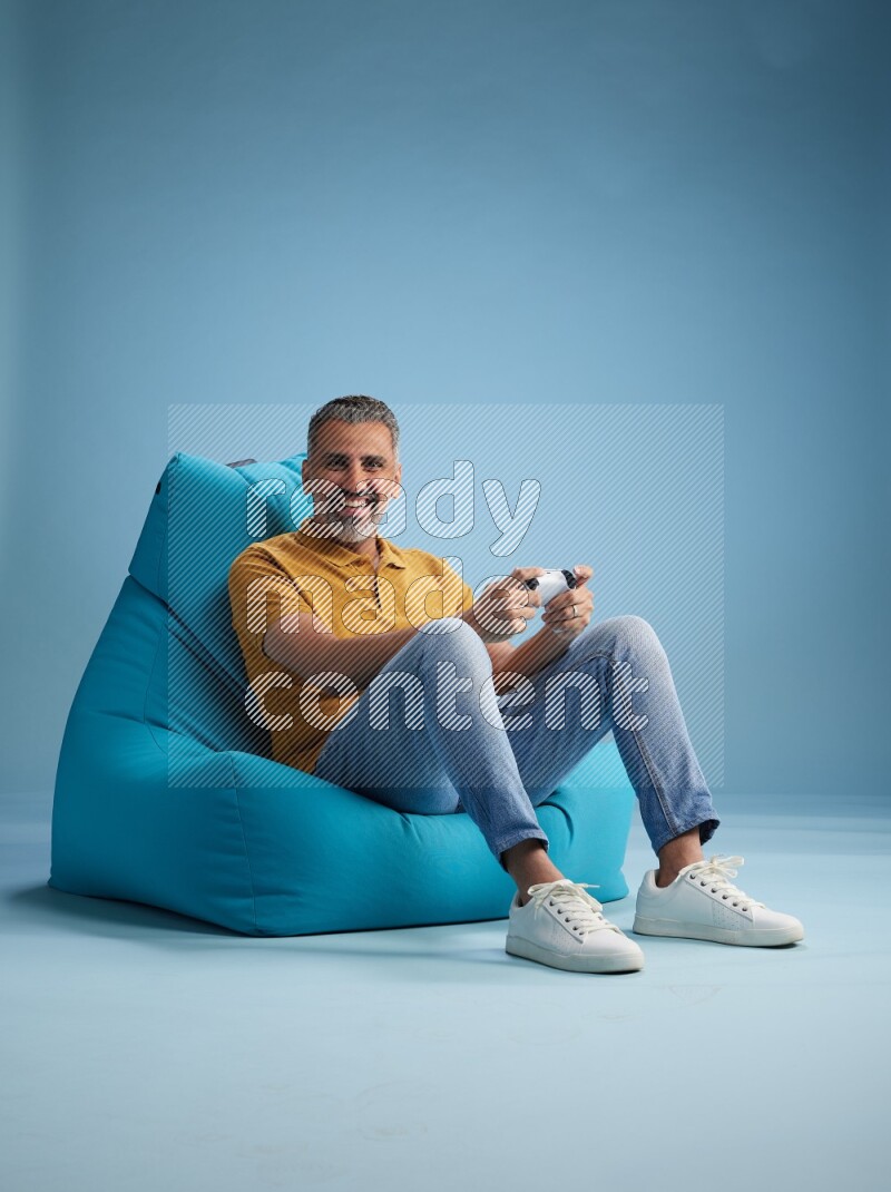 A man sitting on a blue beanbag and gaming with joystick