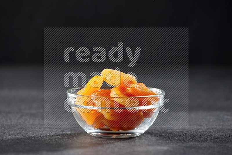 A glass bowl full of dried apricots on a black background in different angles