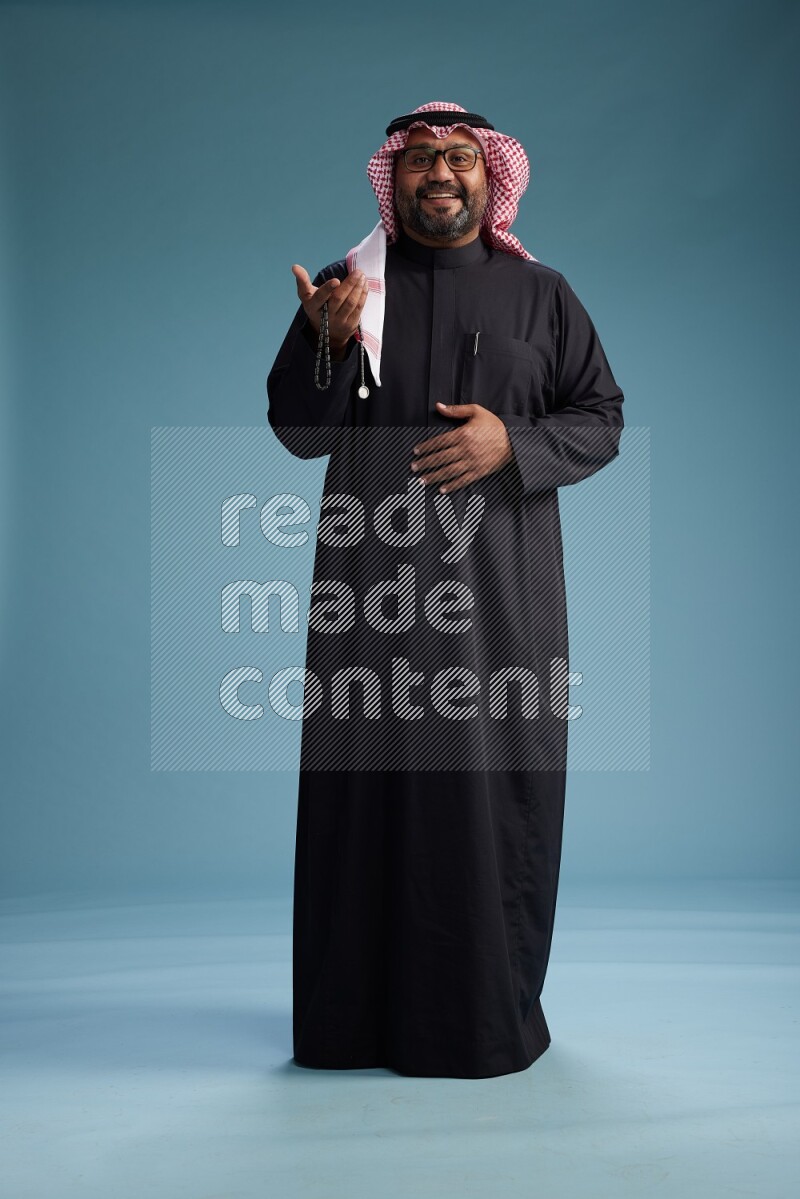 Saudi Man with shimag Standing Interacting with the camera on blue background