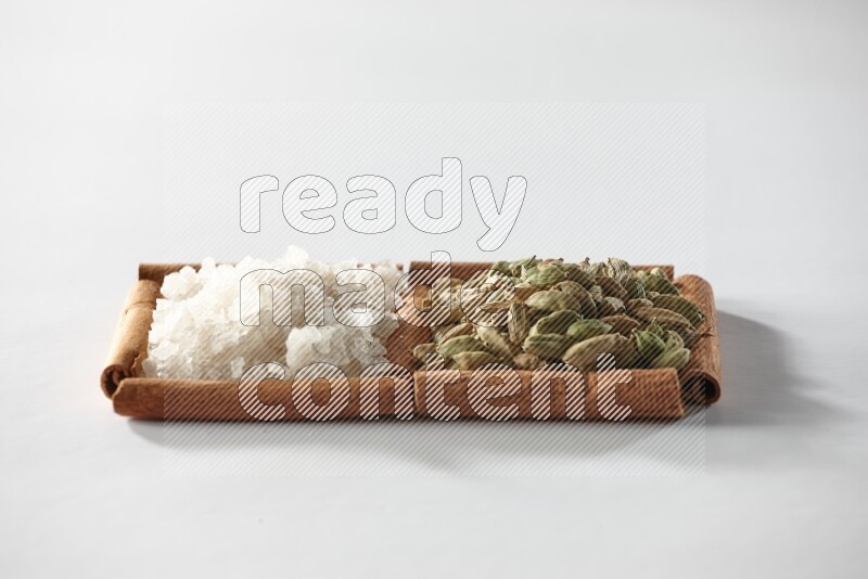 مربعان من أعواد القرفة ممتلئان بحبوب الهيل والملح الأبيض علي خلفية بيضاء