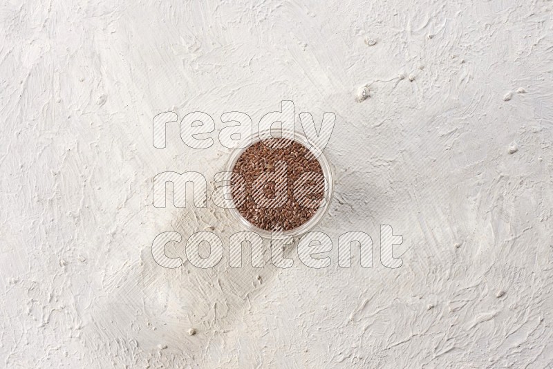 A glass jar full of flax seeds on a textured white flooring