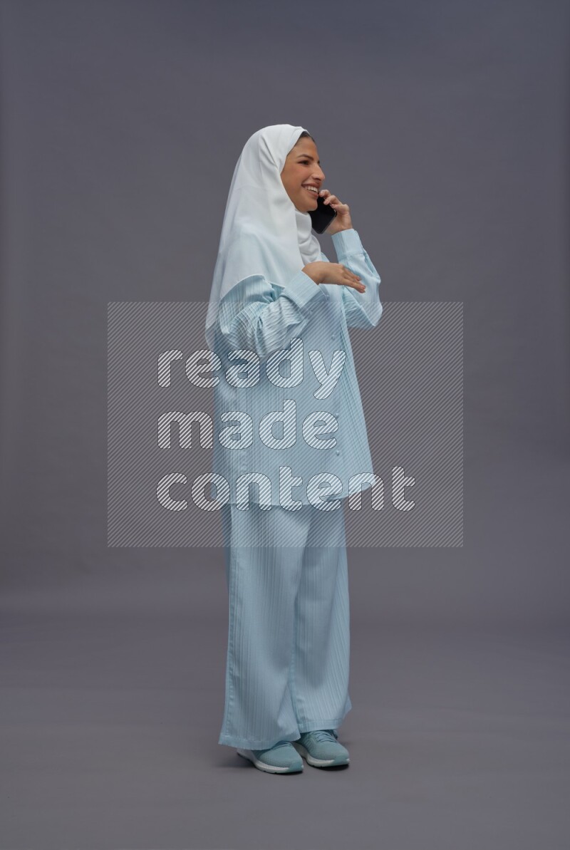 Saudi woman wearing hijab clothes standing talking on phone on gray background