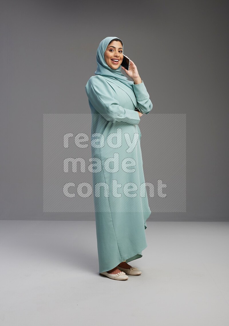 Saudi Woman wearing Abaya standing talking on phone on Gray background