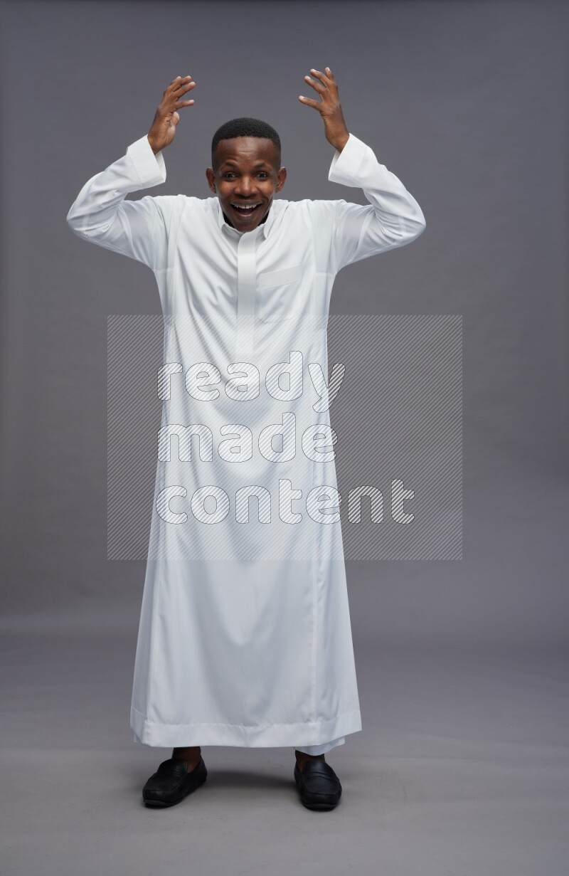 Saudi man wearing thob standing hands behind head on gray background