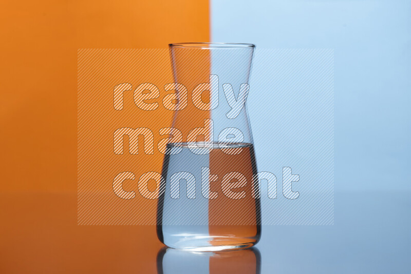 تظهر الصورة أواني زجاجية ممتلئة بالماء موضوعة على خلفية من اللونين البرتقالي والأزرق الفاتح