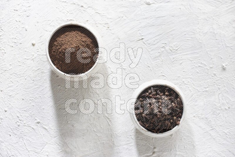 2 Beige ceramic bowls, one full of cloves and the other full of powder on textured white flooring