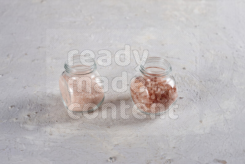 2 glass jars one is filled with fine himalayan salt and the other with coarse himalayan salt on white background