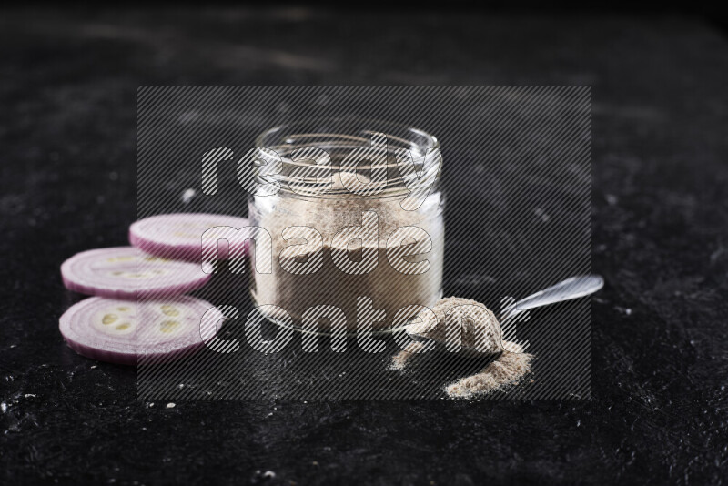 A glass jar full of onion powder on black background