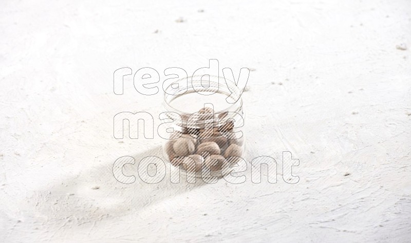 A glass jar full of nutmeg on a white flooring in different angles