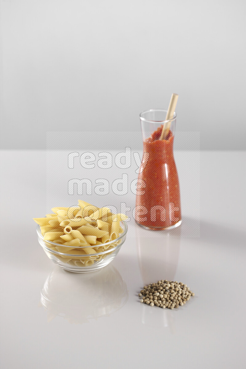 Raw pasta with tomatoe pasta with different ingredients such as cherry tomatoes, basil, garlic, bay laurel, cardamom, white pepper, black pepper, red chilis and wheat stalks on light grey background