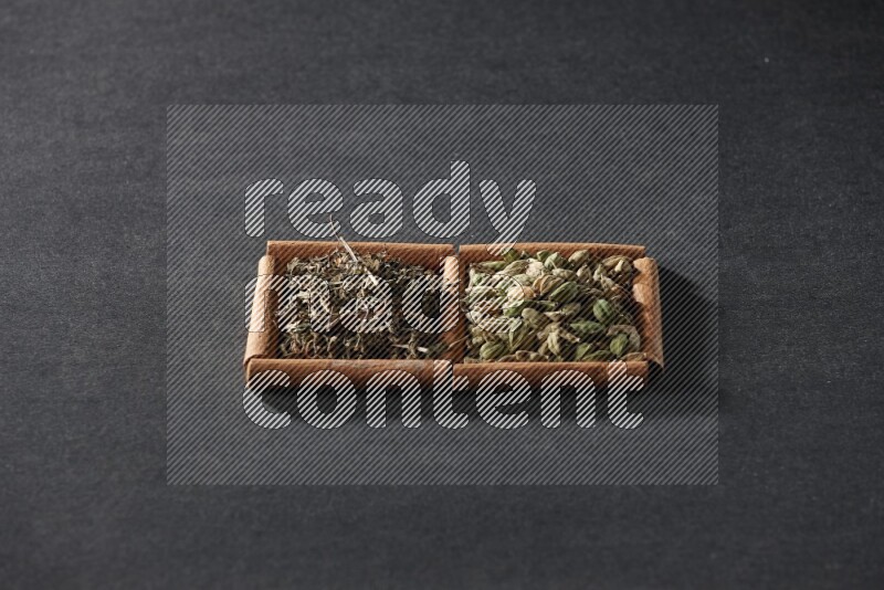 مربعان من أعواد القرفة ممتلئان بحبوب الهيل والريحان المجفف علي خلفية سوداء