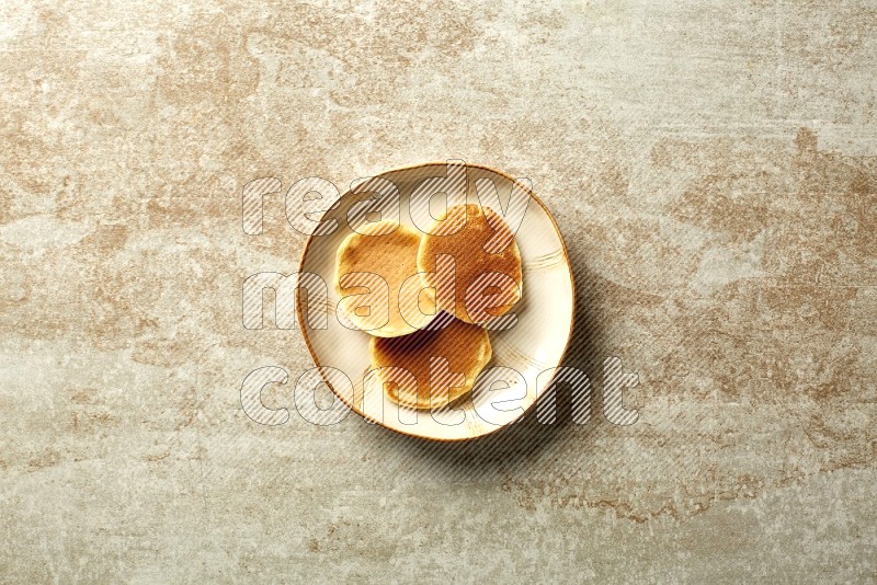Three stacked plain mini pancakes in an irregular plate on beige background