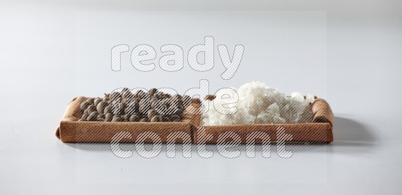 مربعان من أعواد القرفة ممتلئان بالملح الأبيض وحبوب الفلفل الحلو علي خلفية بيضاء