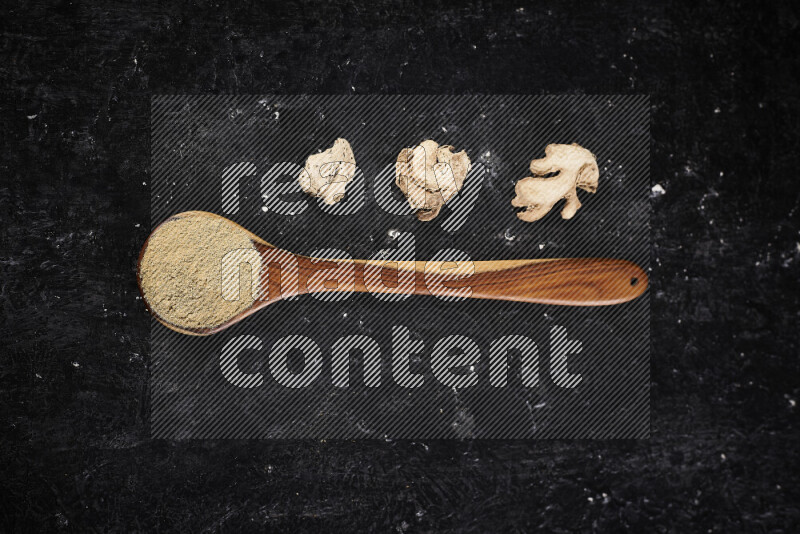 A wooden ladle full of ground ginger powder on black background