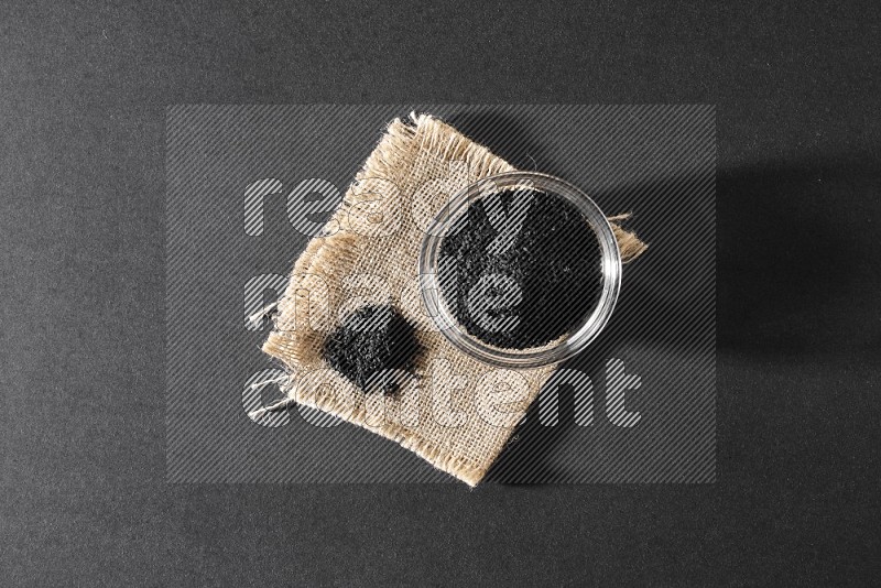 A glass bowl full of black seeds and seeds on burlap fabric on a black flooring in different angles