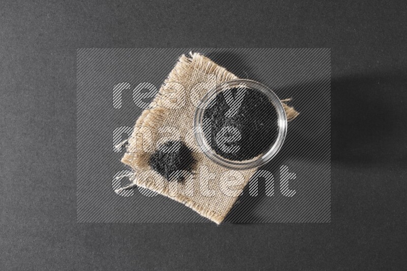 A glass bowl full of black seeds and seeds on burlap fabric on a black flooring