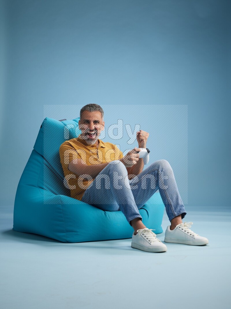 A man sitting on a blue beanbag and gaming with joystick