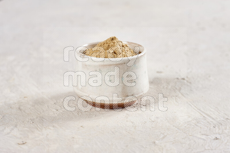 A beige pottery bowl full of ground ginger powder on white background