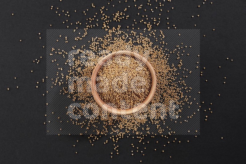 A wooden bowl full of mustard seeds and more seeds spread on a black flooring in different angles